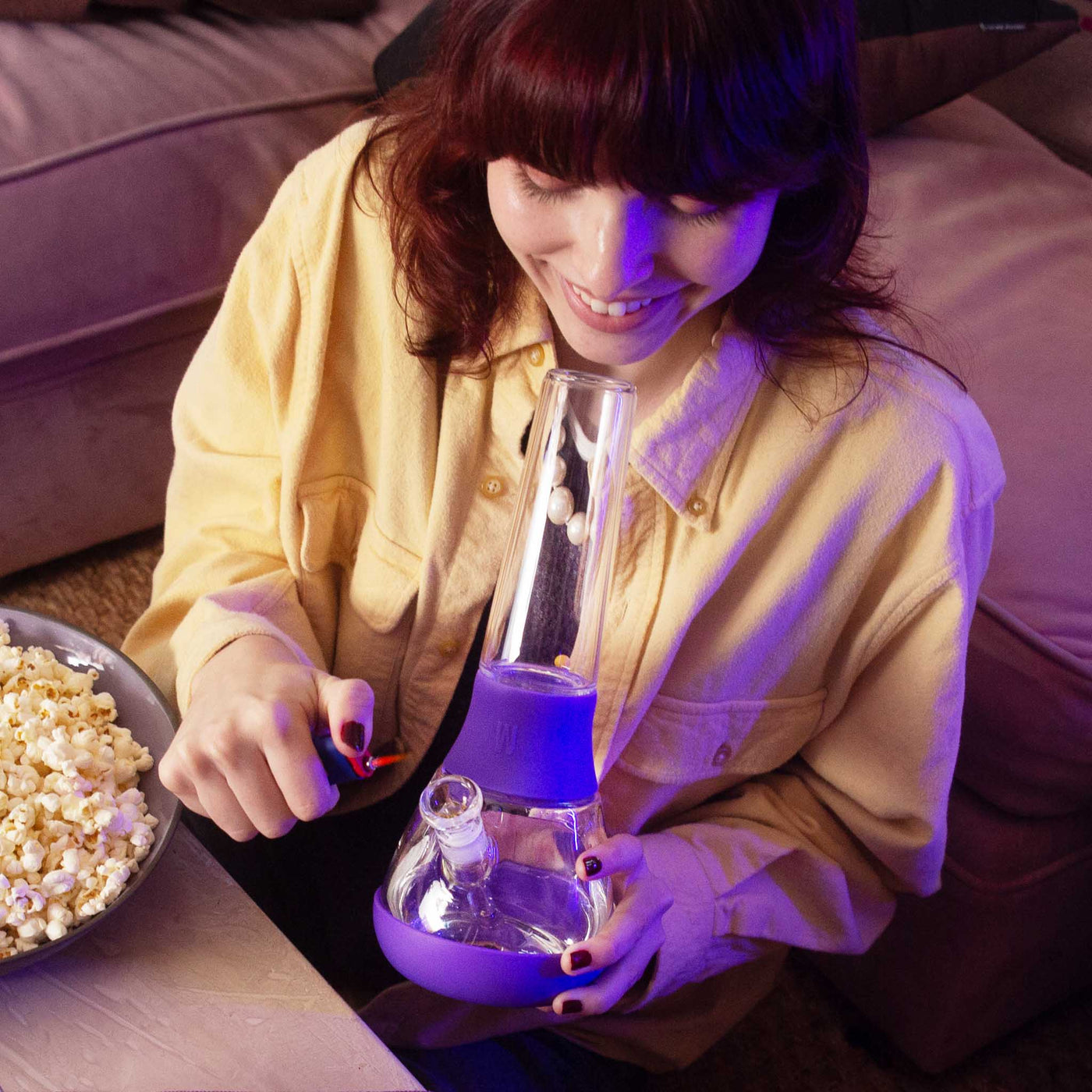 Woman using grape purple bong with bowl of popcorn. 