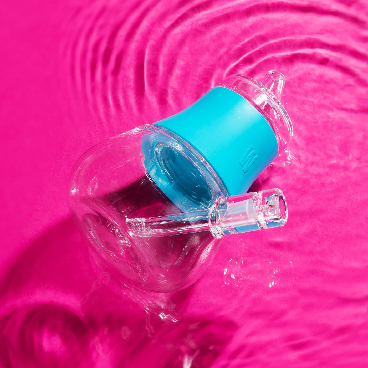 Aqua silicone bubbler top view in a hot pink background with water under