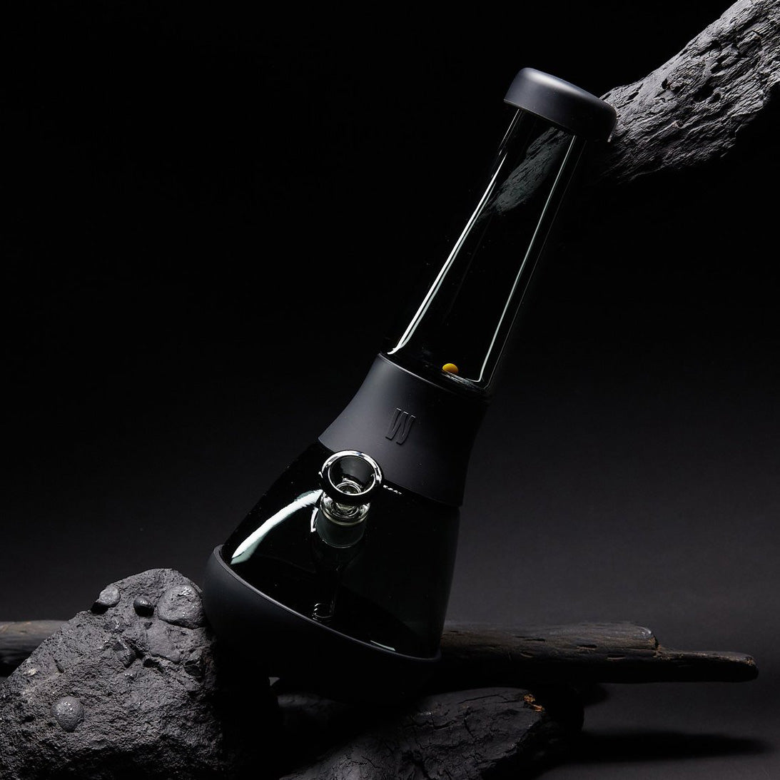 Sleek black glass bong from Weeday resting on rugged stone and wood, showcased against a dark, moody background.