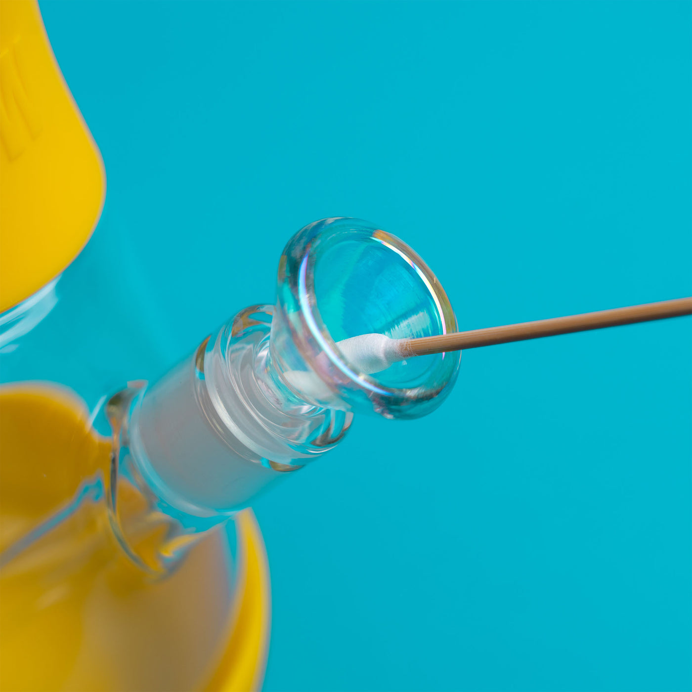 A hand holding the Q tips and cleaning the bong bowl of the yellow bong, blue background 