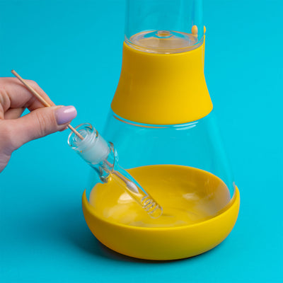 A hand holding the Q tips and cleaning the Downstem of the yellow bong, blue background 