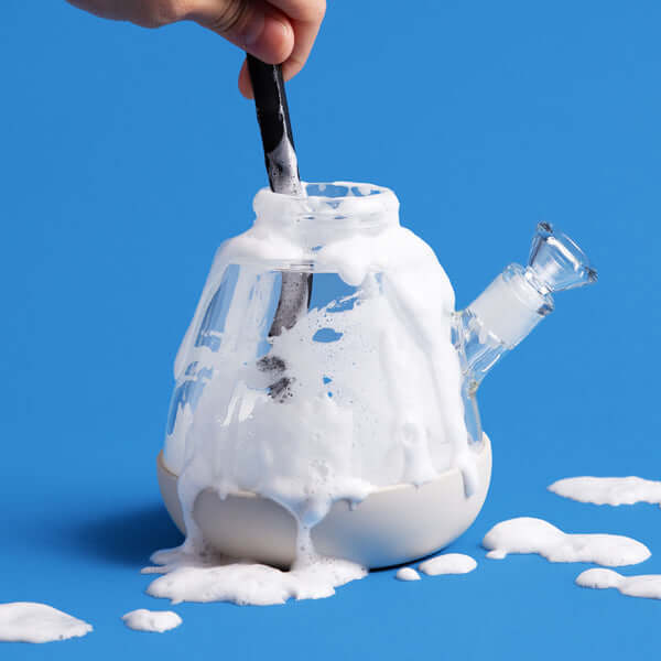 Cleaning bong base and using black cleaning brush to make the bubbles, blue backdrop 