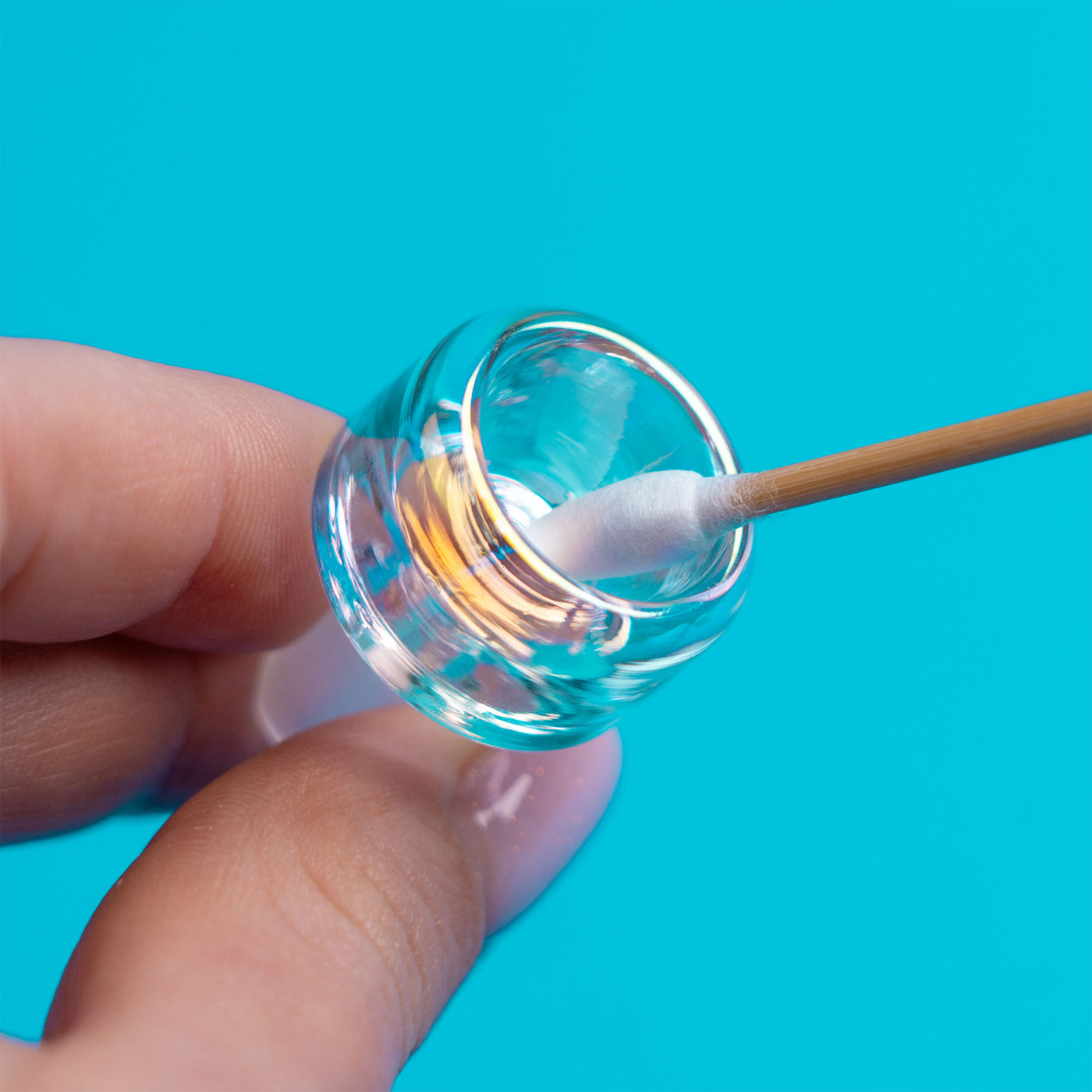 A hand holding iridescent bubbler bowl, and using Q-tip to clean, showing clean glass