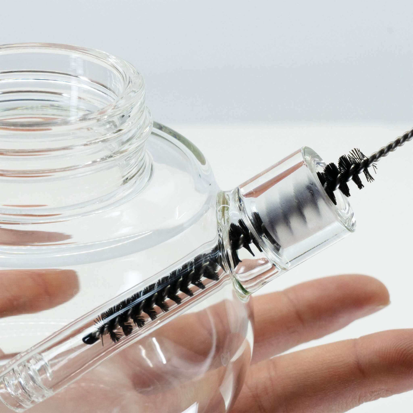 A hand is using downstem brush to clean bubbler base 