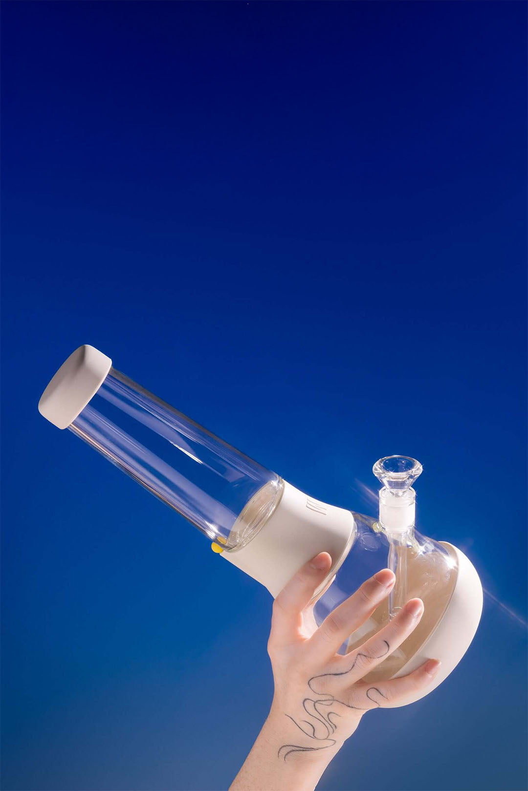 Hand holding up a crystal-like borosilicate glass beaker bong with a cream-white silicone cover against a blue background.