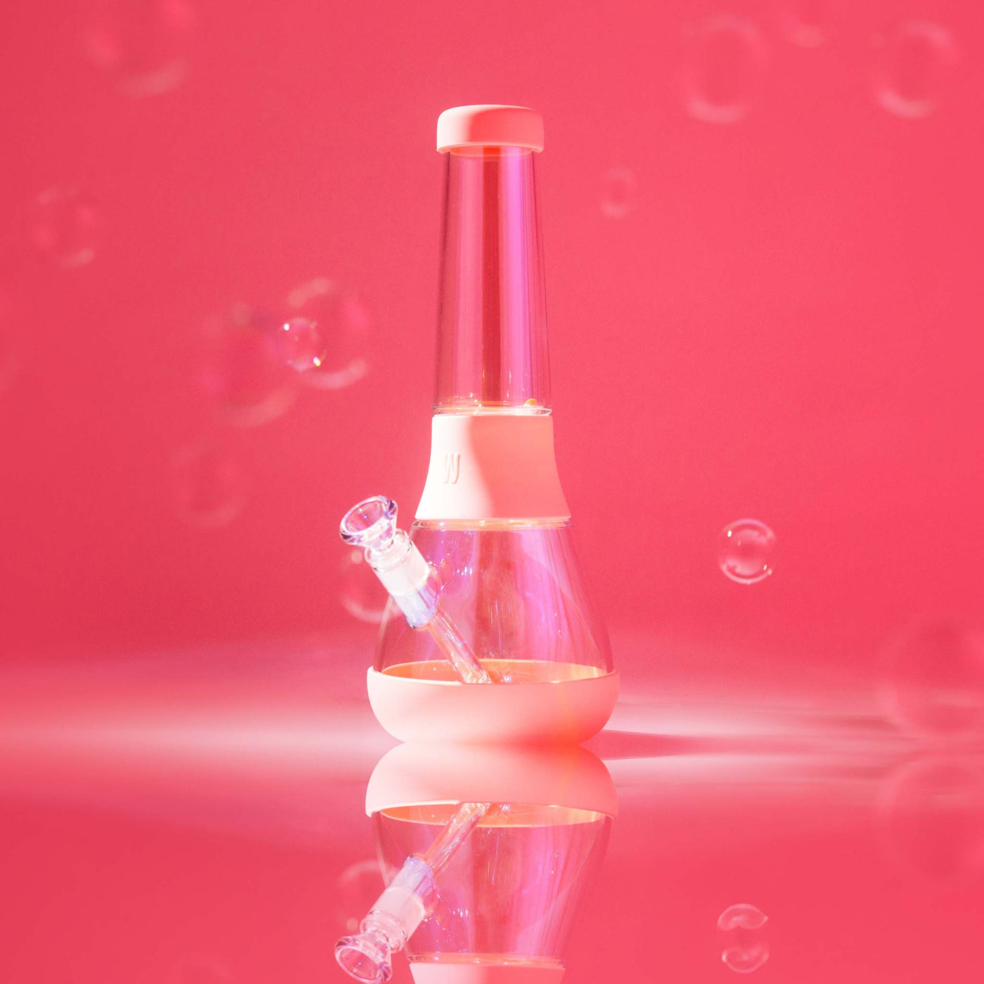 A Bubblegum Pink Iridescent glass bong featuring a reflective studio setup with a vibrant pink backdrop and floating bubbles.