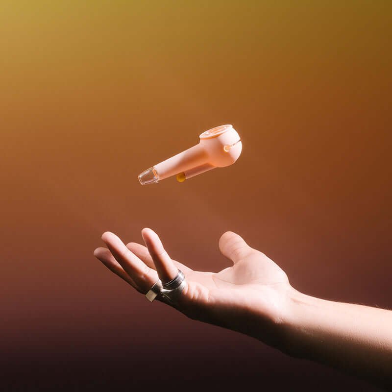 A hand magically lifting a pipe, seemingly floating in the air against an orange, dreamy gradient background.