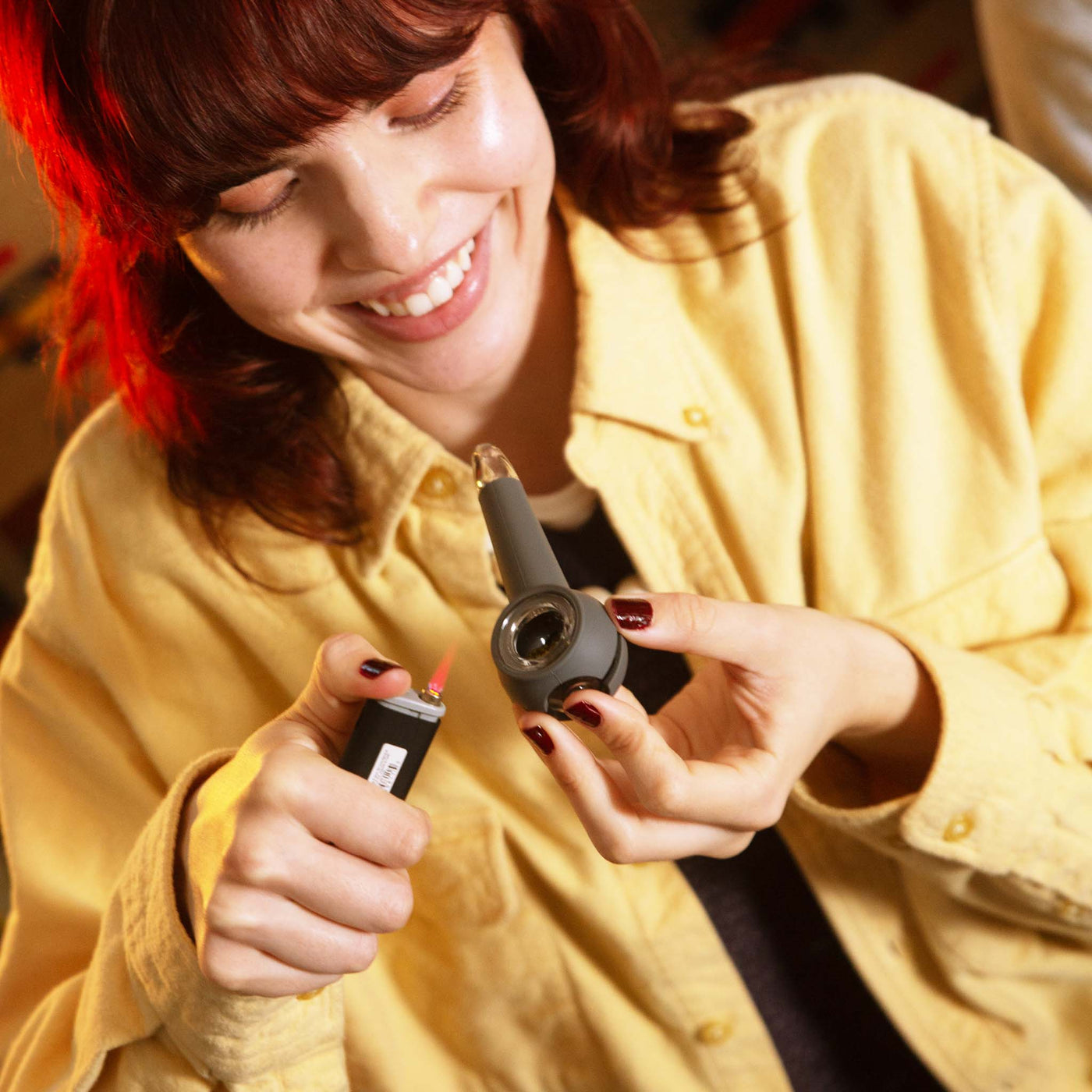 woman in a yellow shirt using a smoke grey pipe with a black lighter.