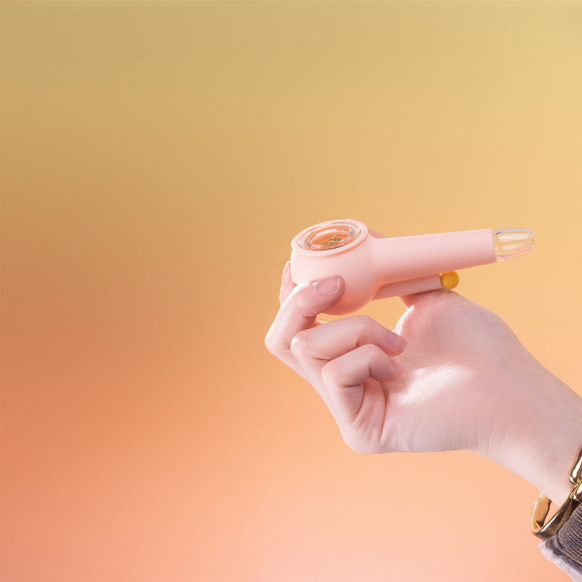 Hand holding a bubblegum pink spoon pipe in front of an orange gradient background.