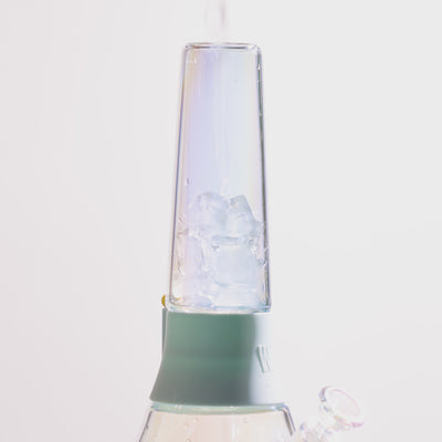 close up of filling iridescent ice catcher bong tube with ice dropping inside, white backdrop 