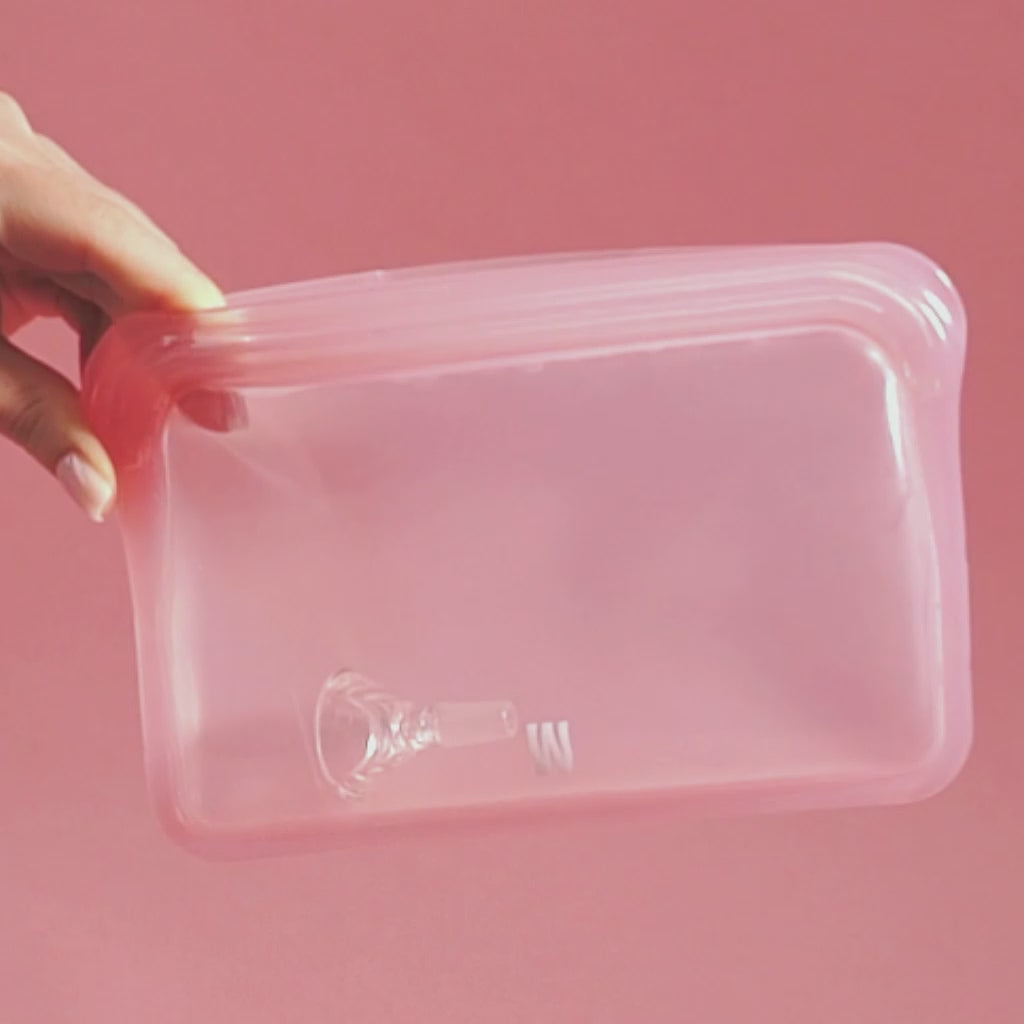 A person is using the pink cleaning pouch, pouring water in, shaking and cleaning the downstem and bowl, pink backdrop