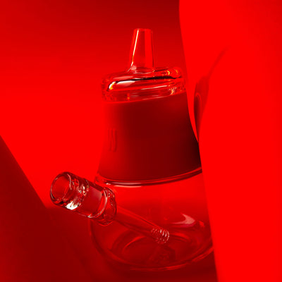 clear glass bubbler with red cover against red background. 