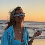 A beautiful model with sunglasses holding her Weeday pipe on a beach during sunset hours.