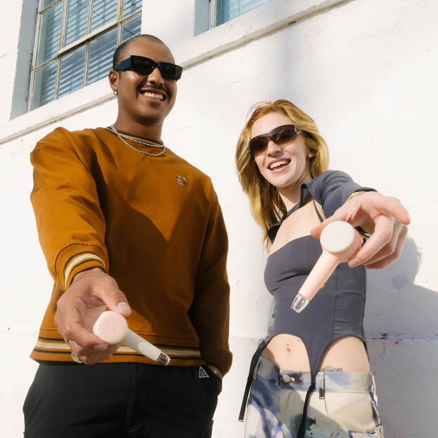 Two person smiling while showing their modular spoon pipe in front of a white wall. It shows the customization feature of the smoke gray hand pipe.