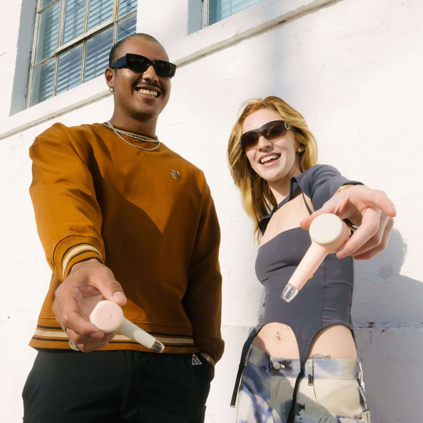 Two person smiling while showing their modular spoon pipe in front of a white wall. It shows the customization feature of the baby pink hand pipe.