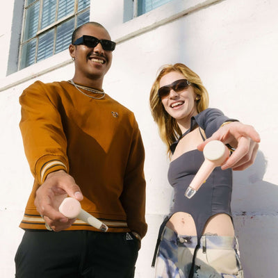 Two person smiling while showing their modular spoon pipe in front of a white wall. It shows the customization feature of the baby pink hand pipe.