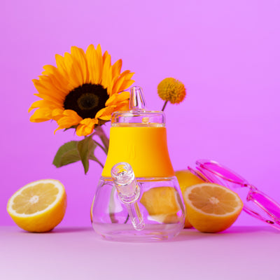 Sunshine silicone bubbler in a pink background with cap aside, flowers and lemons