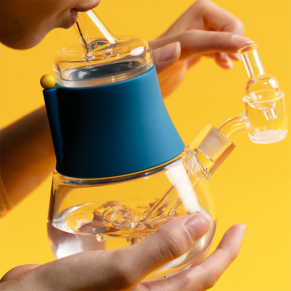 A person holds the dab rig, rotating the cap by hand as water bubbles inside the glass bubbler