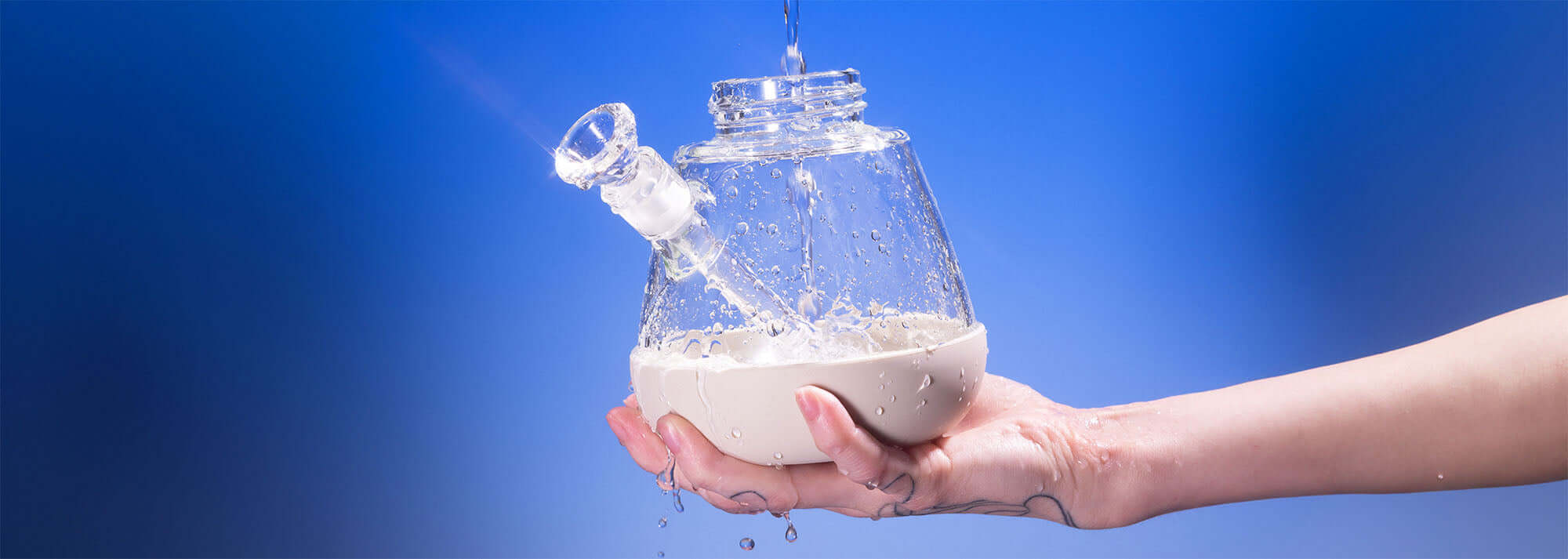 Hand holding the base of a Weeday detachable bong, showing its easy-to-clean design by rinsing under running water against a blue backdrop.