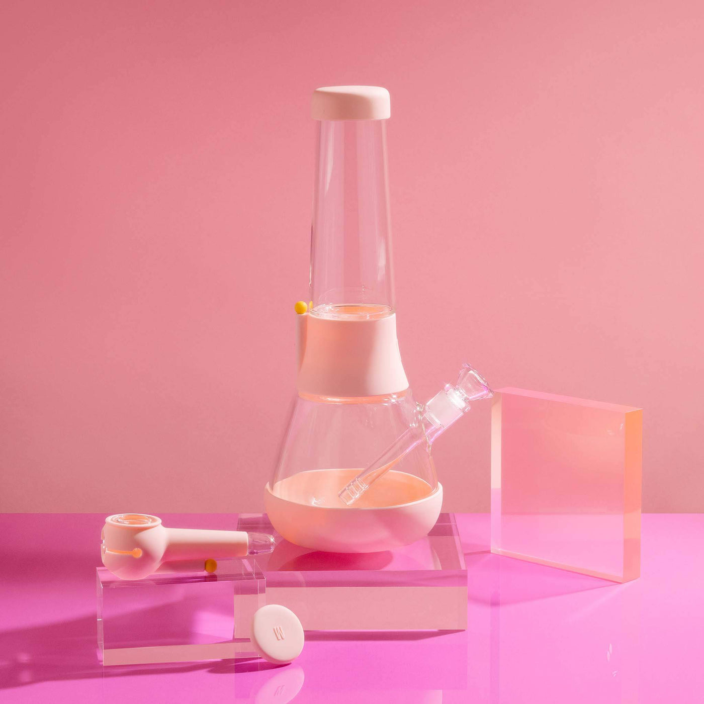  A bundle set of the Weeday beaker bong and silicone pipe with glass bowl, sitting on acrylic blocks, showcased in a bubblegum pink studio setting.