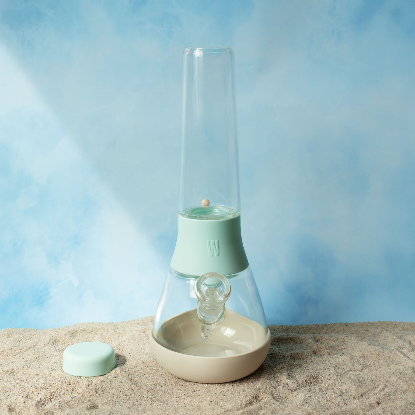 Front view of the Weeday custom bong in Sky and cream mix on sandy surface against a cloudy sky backdrop.