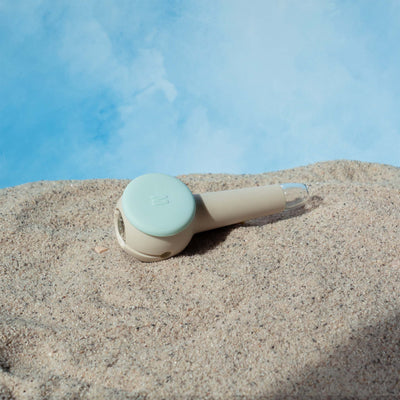 Weeday spoon pipe in sky and cream color mix on sandy surface, against a cloudy sky backdrop.