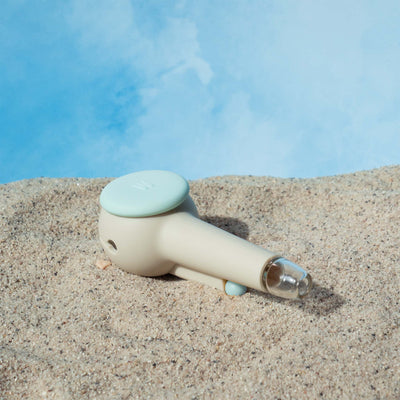 Back view of the Weeday spoon pipe in sky and cream color mix on sandy surface, against a cloudy sky backdrop.