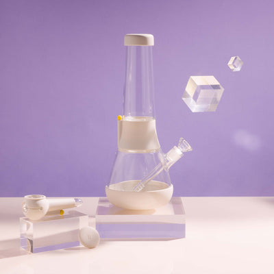  A bundle set of the Weeday beaker bong and silicone pipe with glass bowl, sitting on acrylic blocks, showcased in a cream white studio setting.
