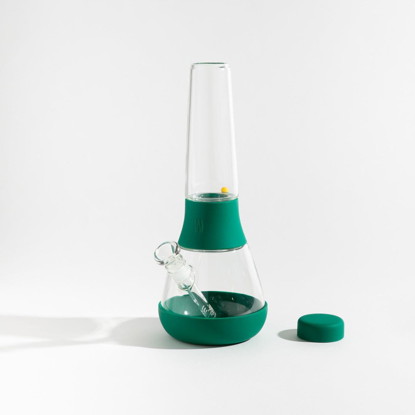 Product photo of a glass waterpipe with forest green silicone covers, cap uncovered, placed on a table.