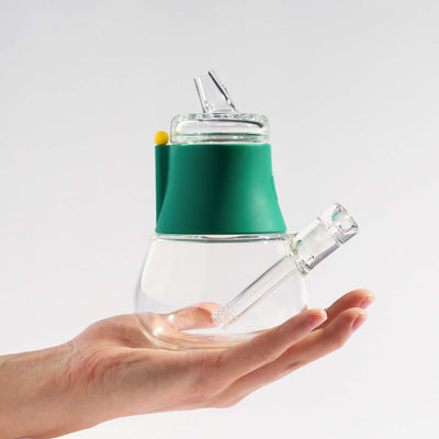 Person holding a compact-sized mini bong with forest green silicone cover on his palm.