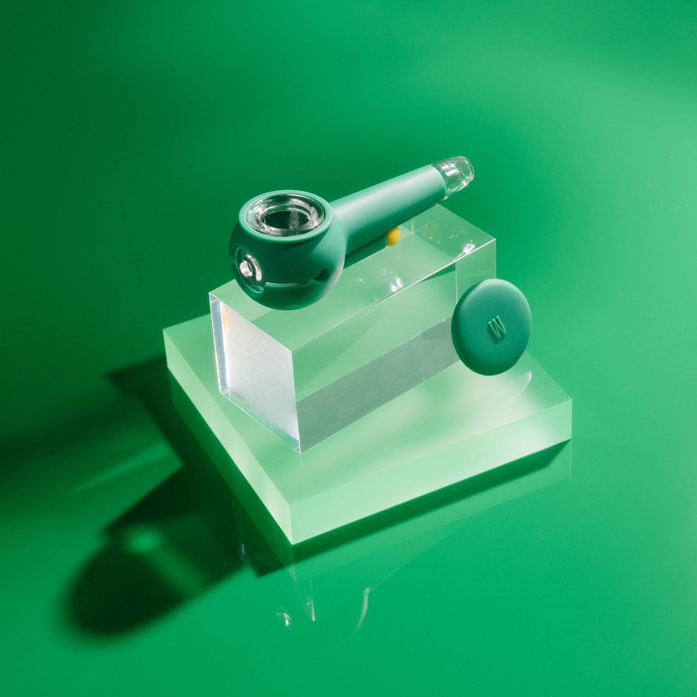 Product photo of a stylish forest green designer pipe on a block of glowing acrylic glass, cap uncovered.