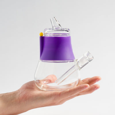 Person holding a compact-sized mini bong with grape purple silicone cover on his palm.