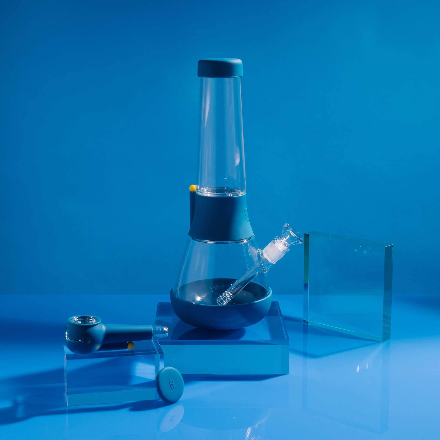  A bundle set of the Weeday beaker bong and silicone pipe with glass bowl, sitting on acrylic blocks, showcased in a midnight blue studio setting.