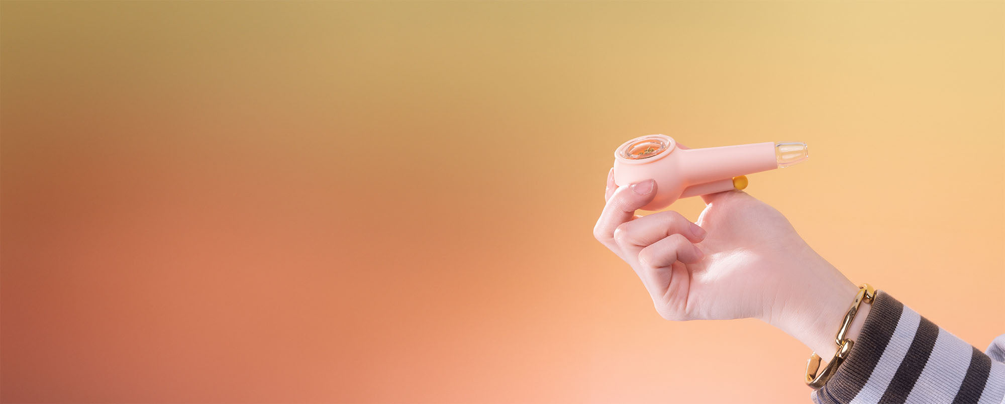 Hand holding a bubblegum pink spoon pipe in front of a wide orange gradient background.