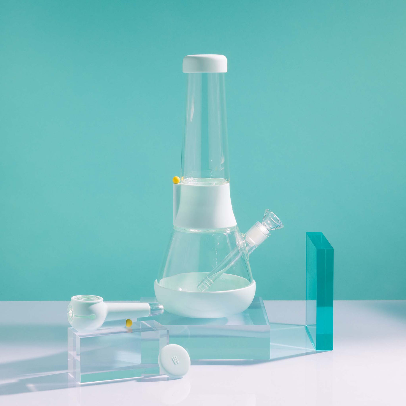  A bundle set of the Weeday beaker bong and silicone pipe with glass bowl, sitting on acrylic blocks, showcased in a sky blue studio setting.