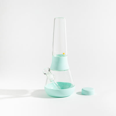 Product photo of a glass waterpipe with sky blue silicone covers, cap uncovered, placed on a table.