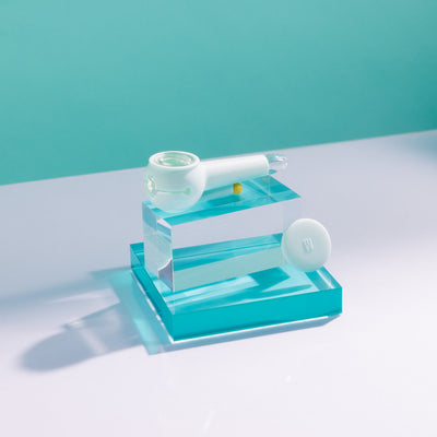 Product photo of a stylish sky blue designer pipe on a block of glowing acrylic glass, cap uncovered.