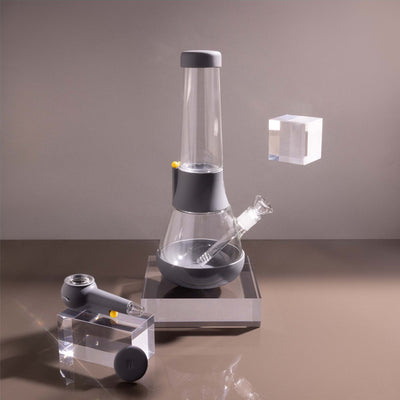  A bundle set of the Weeday beaker bong and silicone pipe with glass bowl, sitting on acrylic blocks, showcased in a smoke gray studio setting.